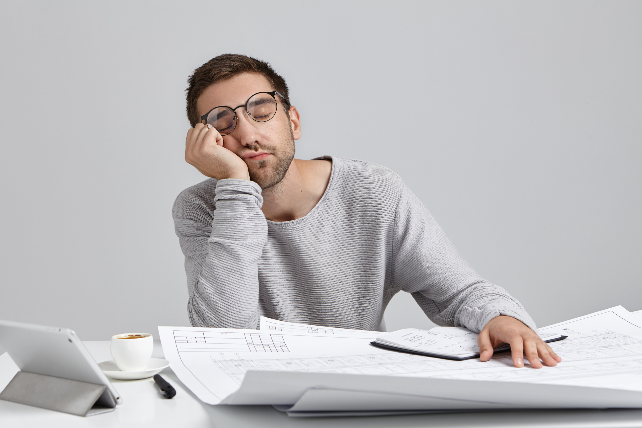 Boredom, fatigue and overwork concept. Funny young bearded male student future architect sleeping at workspace, feeling tired and exhausted while spending sleepless night, working on drawings